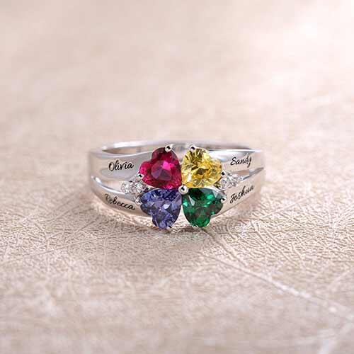 Silver ring with four heart-shaped gems in various colors, engraved with names "Olivia," "Rebecca," "Sandy," "Joshua."