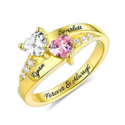 A personalized heart birthstone ring in gold plating with engraved names "Ryan" and "Scarlett," featuring heart-shaped stones and sparkling crystal accents.