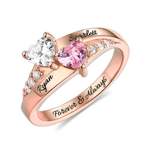 A personalized heart birthstone ring in rose gold plating with engraved names "Ryan" and "Scarlett," featuring heart-shaped stones and sparkling crystal accents.