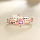 A personalized heart birthstone ring in rose gold plating with engraved names "Ryan" and "Scarlett," featuring heart-shaped stones and sparkling crystal accents.