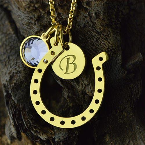 Personalized gold horseshoe necklace with engraved initial disc and birthstone charm, symbolizing luck and protection, perfect for gifting and special occasions.