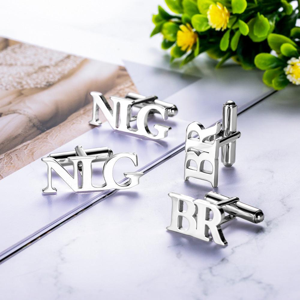 Shiny 'NLG' and 'BR' silver monogram cufflinks arranged on a reflective marble surface.