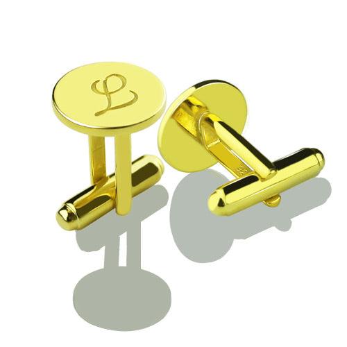 Gold cufflinks with engraved initial 'L' displayed on a reflective surface.