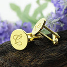 "Gold cufflinks with monogrammed initials 'L' and 'S' on a rustic wooden backdrop with purple flowers.