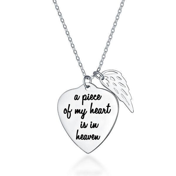 A silver necklace with a heart-shaped pendant engraved with "a piece of my heart is in heaven" and an angel wing charm attached.