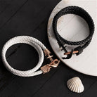 White and black braided bracelets with rose gold and black anchor clasps on a rustic surface.