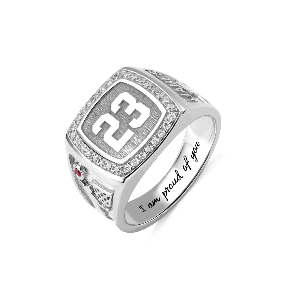 A silver championship ring with the number 23 prominently displayed, surrounded by small diamonds. The side features a red gem and a design, with "I am proud of you" engraved inside.