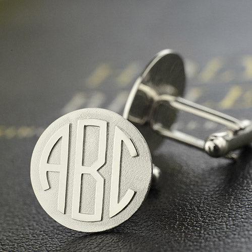 Silver cufflink with 'ABC' monogram, detailed view on a textured black background.