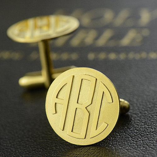 Gold monogram cufflinks with 'ABC' initials, placed on a textured black surface.