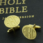 Gold cufflinks with 'ABC' monogram on a black Holy Bible cover.