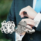 Man adjusting monogrammed cufflinks with intricate silver designs on his shirt sleeve.