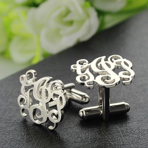 Silver monogram cufflinks with an intricate design displayed against a floral backdrop.