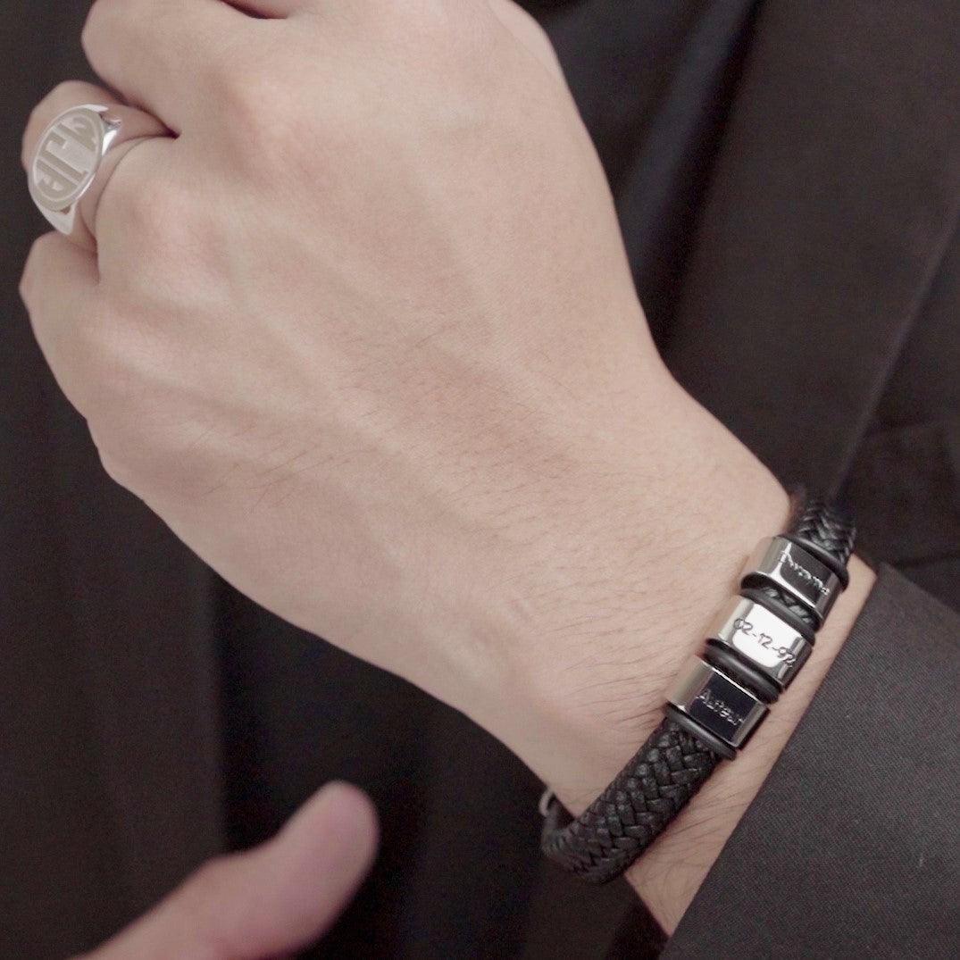 Close-up of a hand wearing a black leather bracelet paired with a monogrammed signet ring.