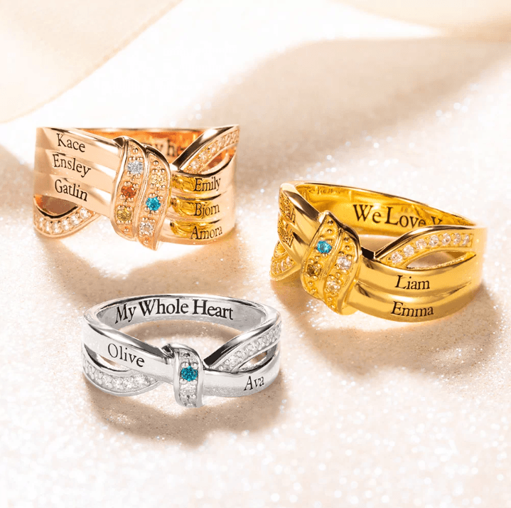 Three intertwined rings with names engraved on them in gold, rose gold, and silver, adorned with small gemstones and the phrases "My Whole Heart" and "We Love U."