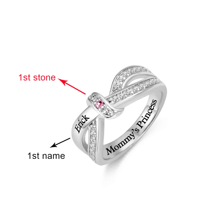 A silver intertwined ring with a pink gemstone and the name "Erick" engraved on one band. The other band is engraved with "Mommy's Princess."