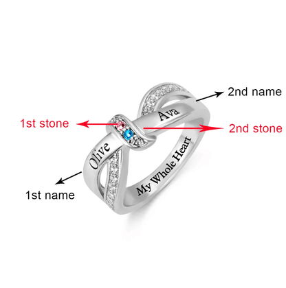 A silver intertwined ring with pink and blue gemstones, engraved with the names "Olive" and "Ava" on each band and the phrase "My Whole Heart."