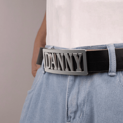 Close-up of a silver belt buckle with 'DANNY' in bold letters on a person wearing a white shirt and blue jeans.