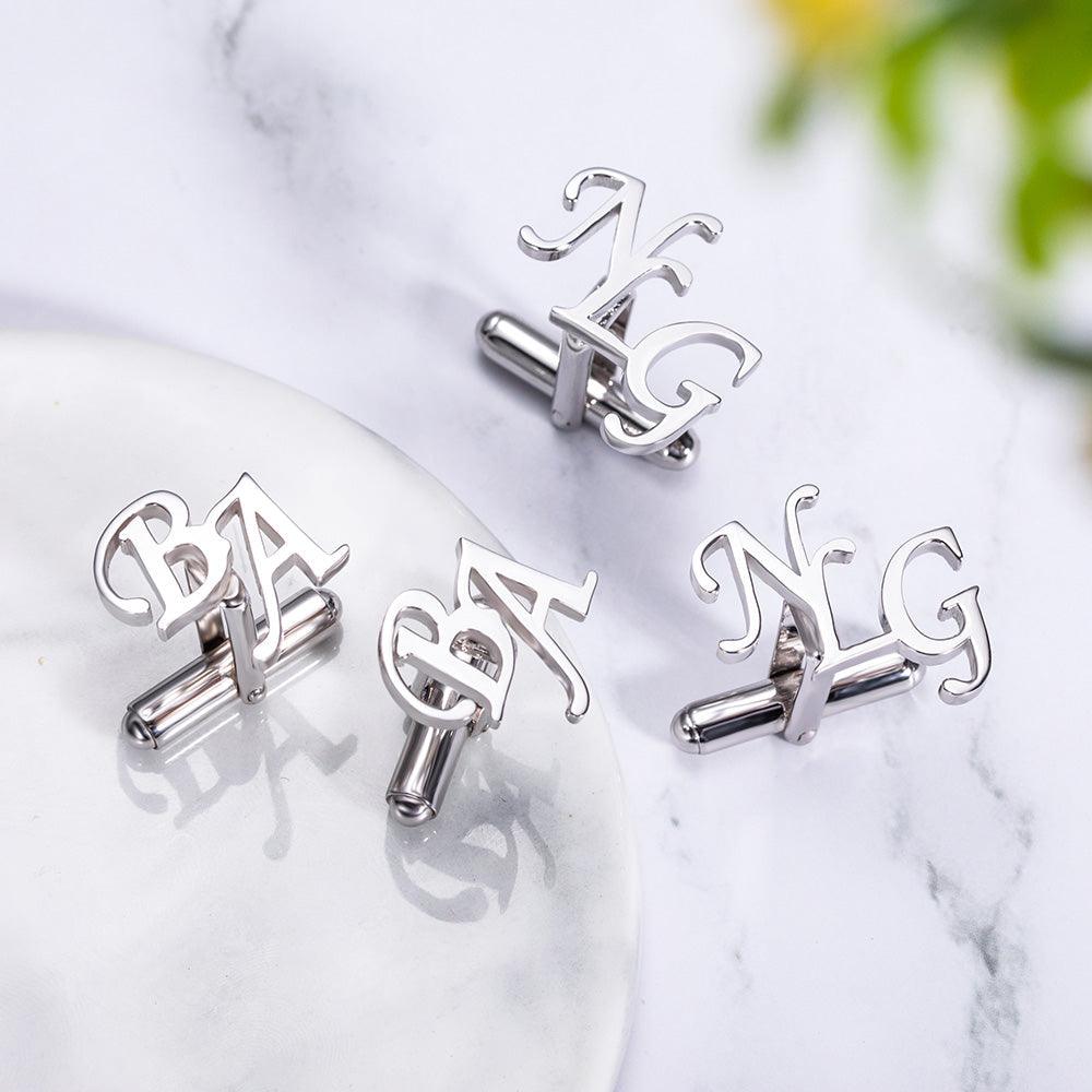 Silver cufflinks with intricate 'NG' and 'BA' initials displayed on a marble surface with a subtle floral background.