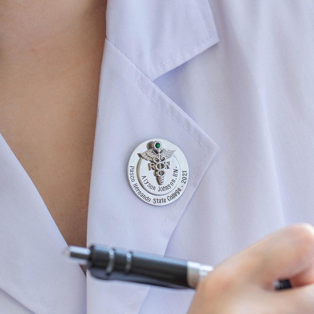 Nurse's white coat with a personalized RN nursing pin adorned with a green gem.