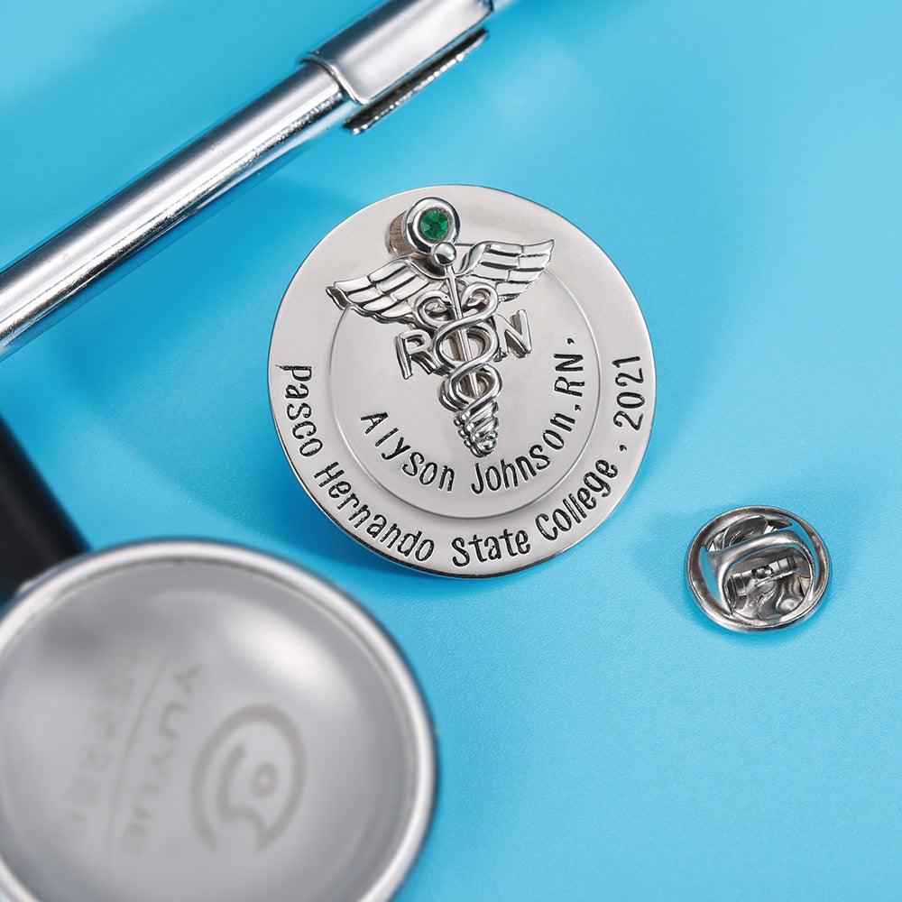 Custom RN nursing pin with a green gem beside a stethoscope on a blue surface.