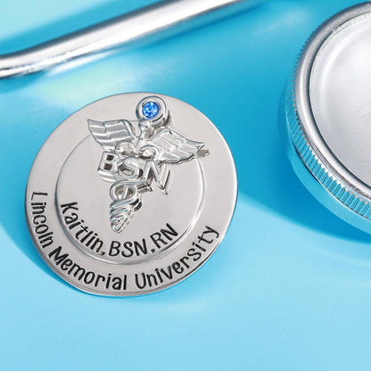 Silver BSN nursing pin with blue gem next to a stethoscope on blue background.