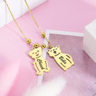 A gold necklace with two pendants shaped like a dog and a cat on a pink background. The dog pendant is engraved with "Cheech" and the cat pendant with "Bella."