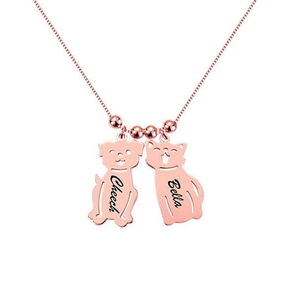 A rose gold necklace with two pendants shaped like a dog and a cat. The dog pendant is engraved with "Cheech" and the cat pendant with "Bella."