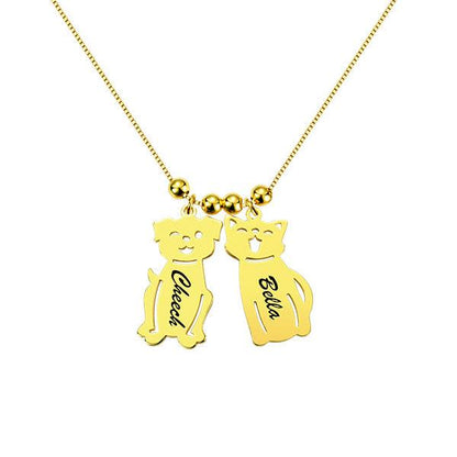 A gold necklace with two pendants shaped like a dog and a cat. The dog pendant is engraved with "Cheech" and the cat pendant with "Bella."