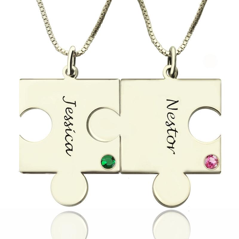 Two interlocking puzzle piece necklaces, one labeled "Jessica" with a green gem, and the other labeled "Nestor" with a pink gem.