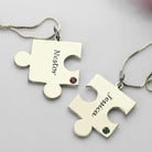 Two silver puzzle piece necklaces on a white background, one labeled "Nestor" with a red gem and the other labeled "Jessica" with a green gem.