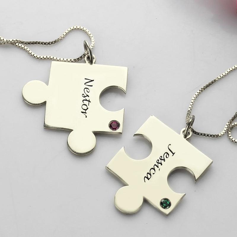 Two silver puzzle piece necklaces on a white background, one labeled "Nestor" with a red gem and the other labeled "Jessica" with a green gem.