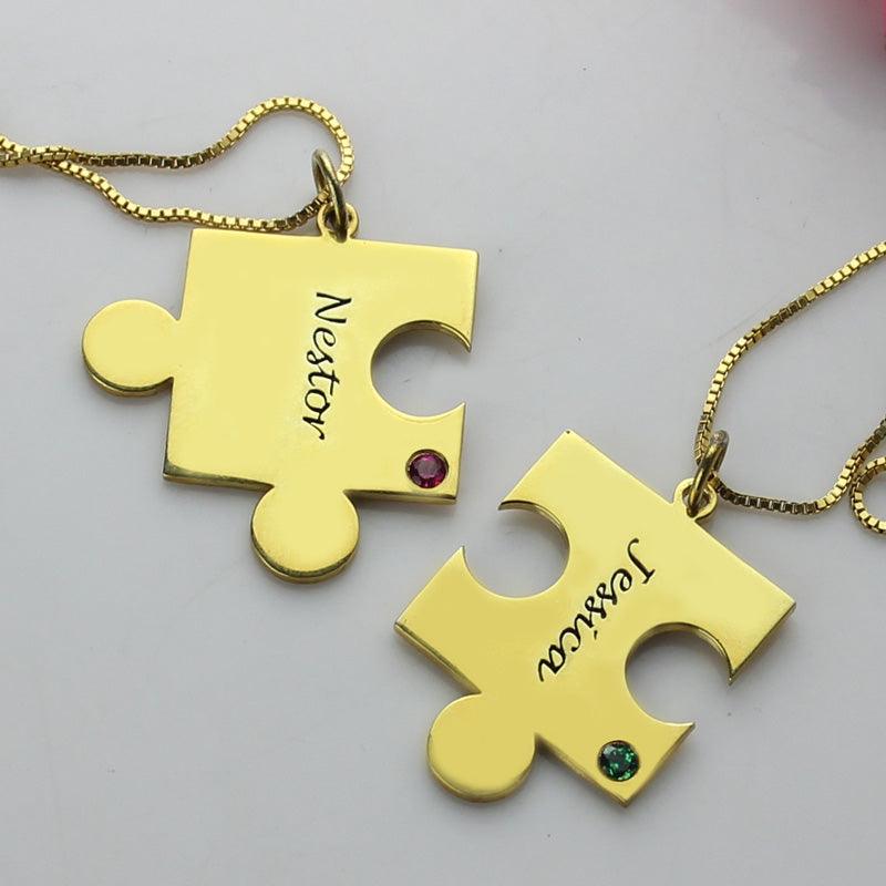 Two gold puzzle piece necklaces on a white background, one labeled "Nestor" with a red gem and the other labeled "Jessica" with a green gem.