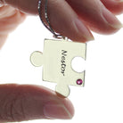 Close-up of a hand holding a silver puzzle piece necklace labeled "Nestor" with a red gem.