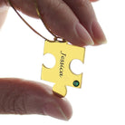 Close-up of a hand holding a gold puzzle piece necklace labeled "Jessica" with a green gem.