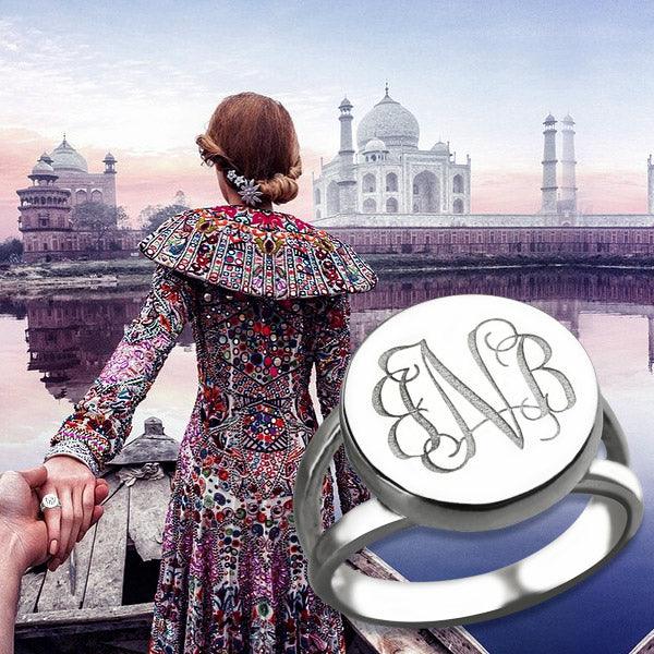 A woman in a colorful, intricately patterned dress holding hands in front of the Taj Mahal, with a silver ring featuring a semi-split shank band and engraved initials "ENB" in the foreground.