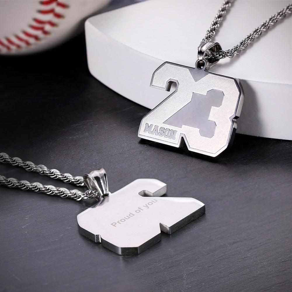 Two silver pendants with the number 23, one engraved with "Mason" and the other with "Proud of you," hanging from silver chains, placed near a baseball.