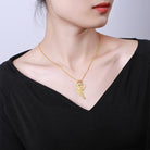 Woman wearing a delicate gold winged-heart necklace against a black top