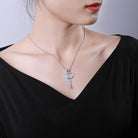 Woman wearing a silver winged-heart necklace with rhinestones, against a black blouse.