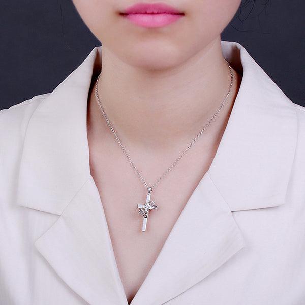 A person wearing a silver cross pendant with a solid design and a ring inscribed with "FAITH." The pendant hangs from a silver chain over a light-colored blouse.