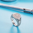 A silver ring with an engraved medical symbol and the year "2017." The ring is inscribed with "Healing hands" and displayed against a blue background with medical tools.