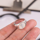 A close-up of a hand holding a silver ring engraved with a caduceus symbol and the year "2021." The ring is inscribed with "We're proud of you."