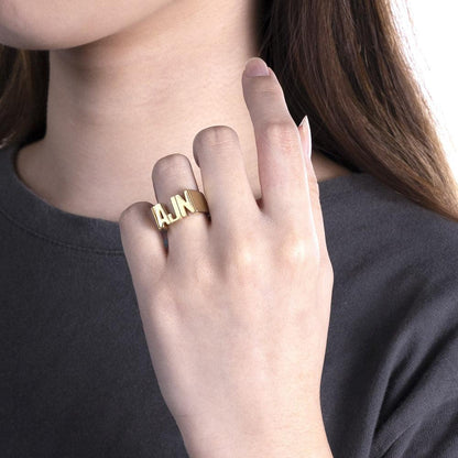 A person wearing a gold custom name ring with the initials 'AJN,' showcasing the ring on their finger against a dark shirt.