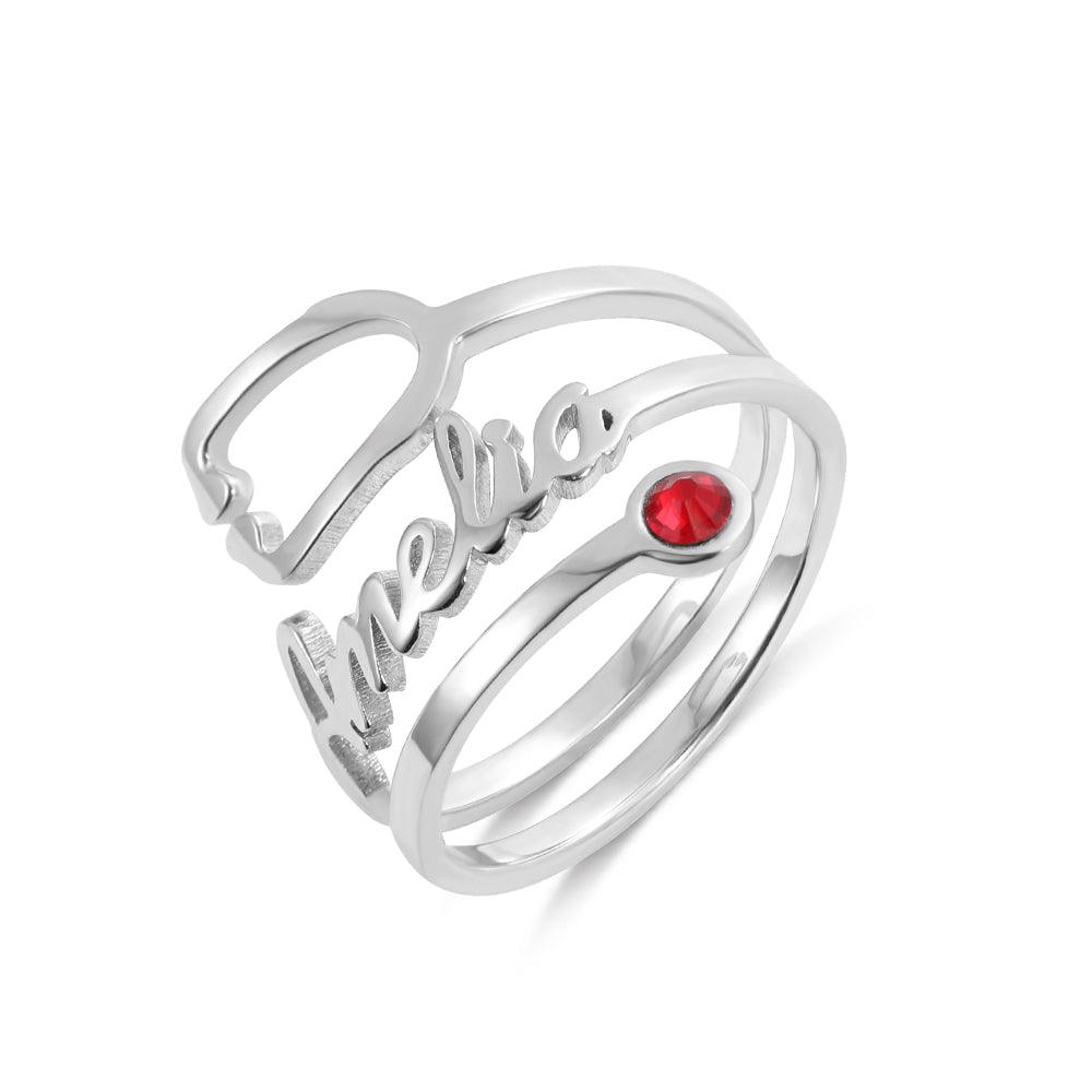 A silver ring with the name "Amelia" written in cursive, featuring a red gemstone set in the middle of one of its bands.