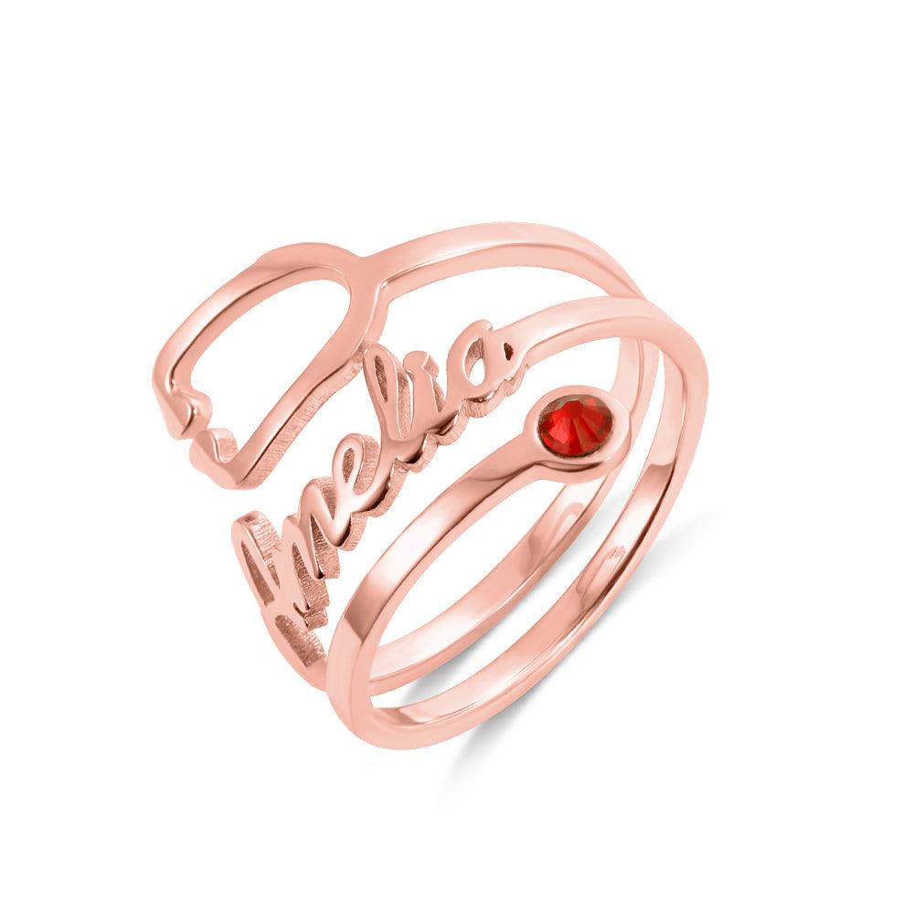 A rose gold ring with the name "Amelia" written in cursive, featuring a red gemstone set in the middle of one of its bands.