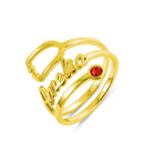 A gold ring with the name "Amelia" written in cursive, featuring a red gemstone set at the end of one of its bands.