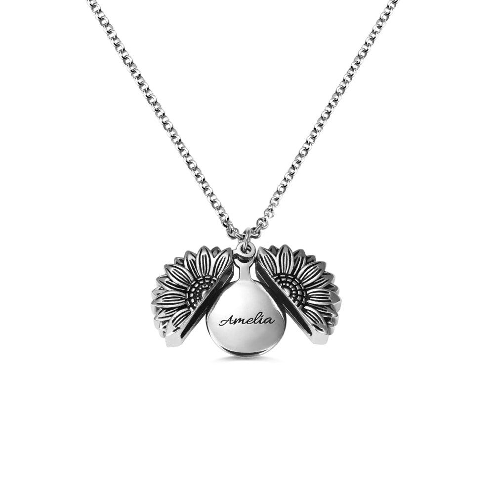 A silver sunflower-shaped locket necklace, opened to reveal the name "Amelia" engraved inside, displayed against a white background.