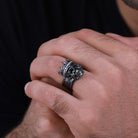 Man's hand with a dark-toned skull ring featuring a crown and crystal accents.