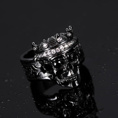 Dark-toned skull ring with jeweled crown reflecting on a water-droplet surface.