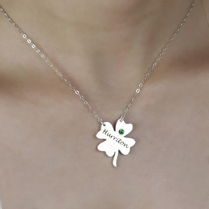 A silver necklace with a four-leaf clover pendant inscribed with "Huririton" and a green gemstone, worn around a person's neck.