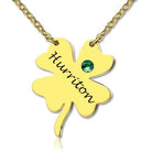 A gold necklace with a four-leaf clover pendant inscribed with the name "Huririton" and a green gemstone embedded in one of the leaves.